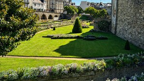 Un patio histórico con muros de piedra, un césped central y una gran variedad de plantas con flores.
