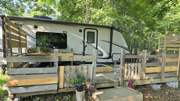 A recreational vehicle (RV) parked in a wooded area with a wooden fence and steps leading to the entrance.