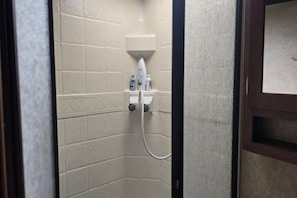 A small, enclosed shower area with a white tiled wall, a handheld showerhead, and a soap dispenser.