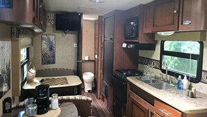A compact RV kitchen with a stove, sink, and a television mounted on the wall.