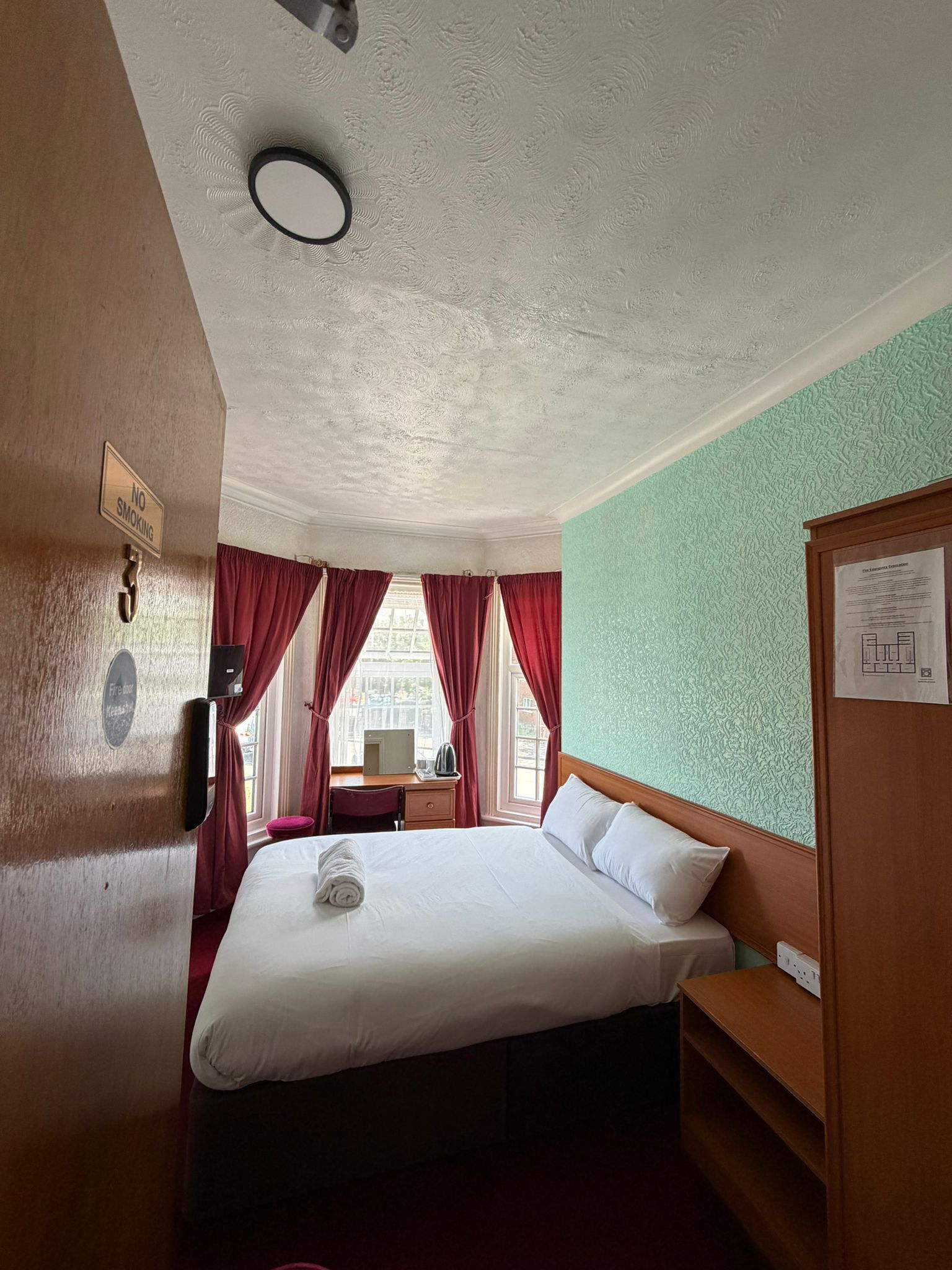 Habitació d'hotel amb llit, escriptori i finestra amb cortines.