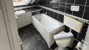 A bathroom with a bathtub, toilet, and sink, featuring black marble tiles and a white vanity. - Fjaerland Hotel (Great Yarmouth)