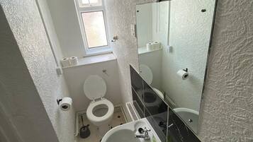 A bathroom with a white sink, a mirror, a toilet, and a window.
