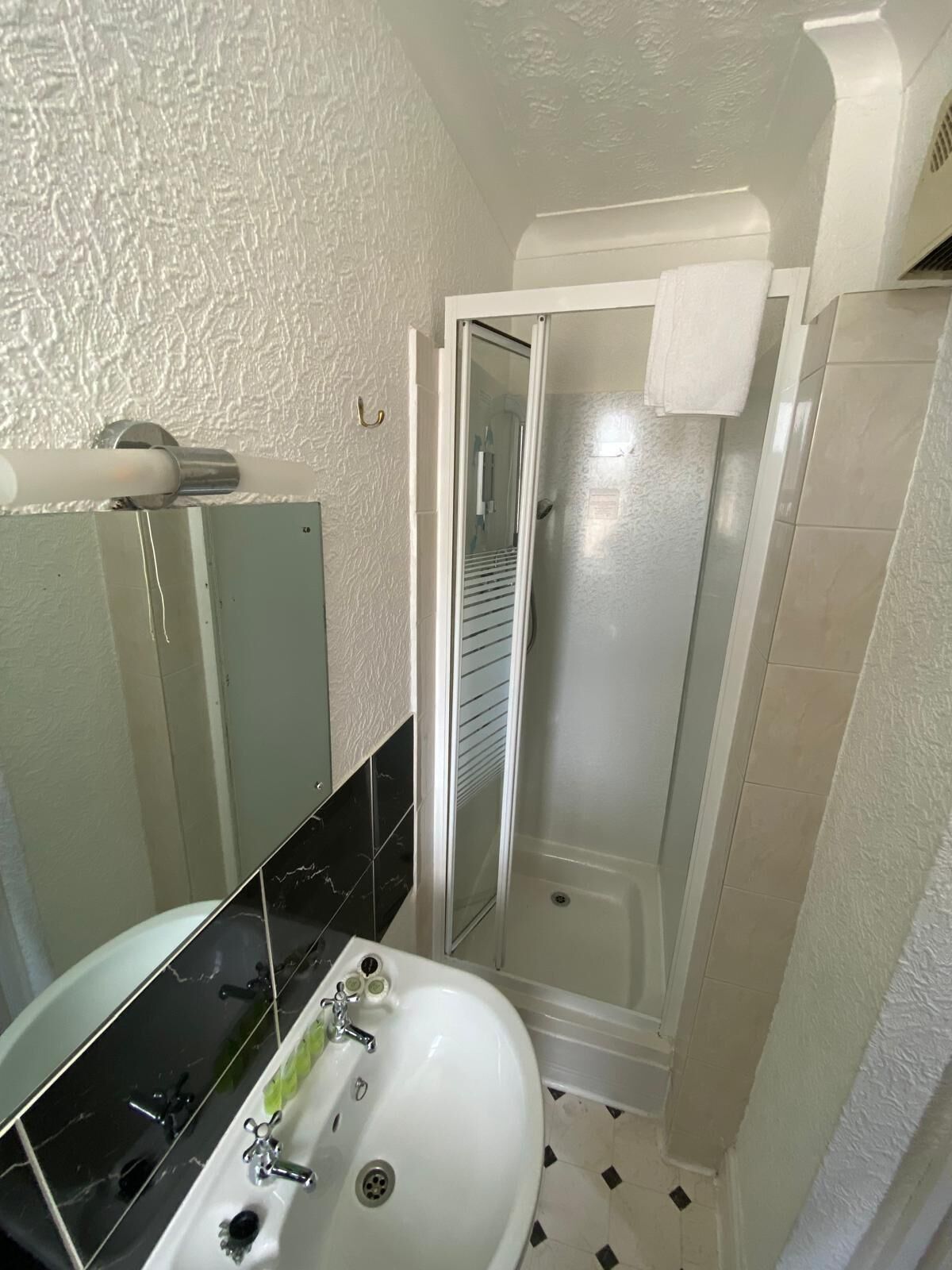 Un baño con un lavamanos blanco, un espejo, cabina de ducha y suelo de baldosas.