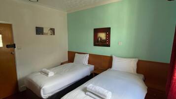 Habitación de hotel con dos camas, cabecero de madera, una puerta y un muro con dos cuadros enmarcados.
