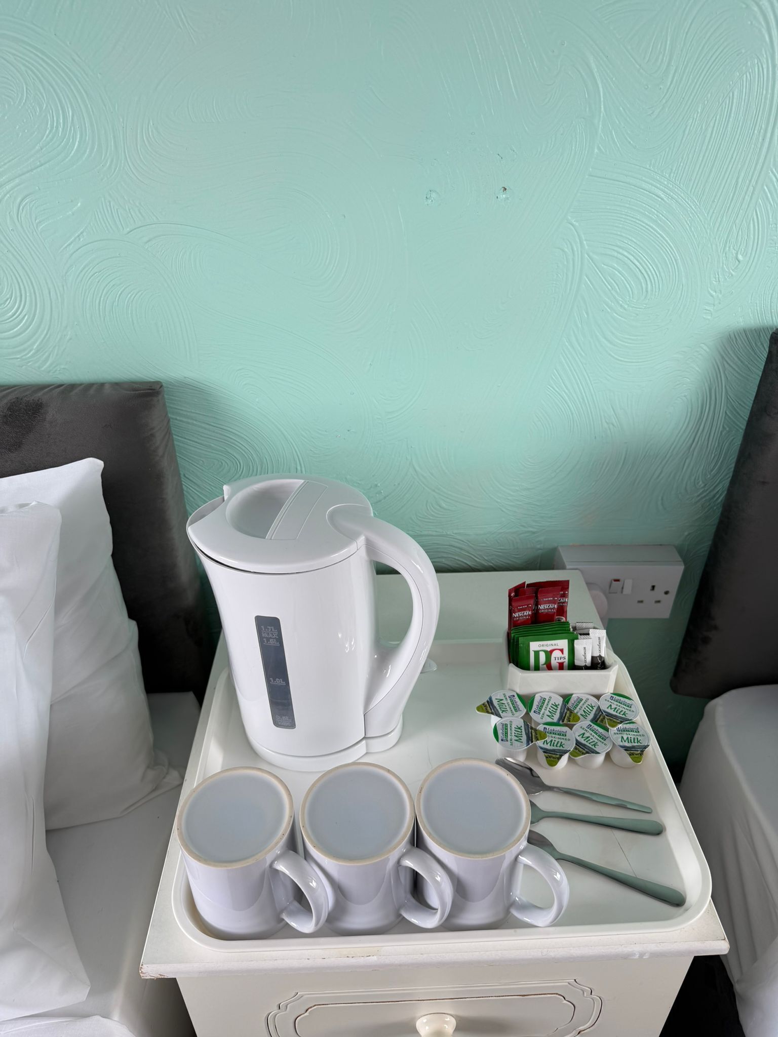 A white tray with a kettle, four mugs, a box of Nescafé coffee capsules, and a milk carton.