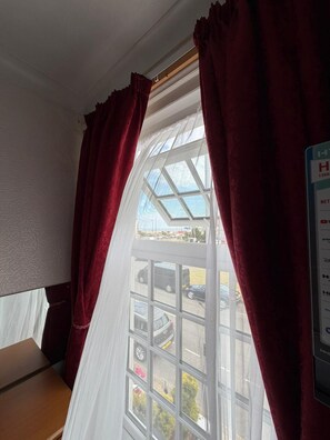 Una habitación con un ventanal grande, cortinas rojas y vista a coches estacionados afuera.