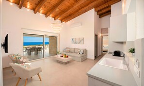 A modern living room with a sofa, a dining area with a table and chairs, a kitchen with a sink, and a view of the sea through large windows. - Vista Mare Villa Heated Pool (Dramia)