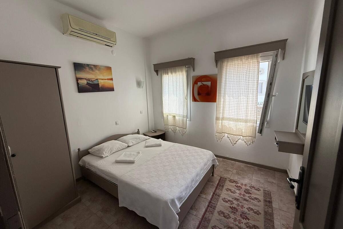 A bedroom with a bed, a nightstand, an air conditioner, a painting, and a window with curtains.