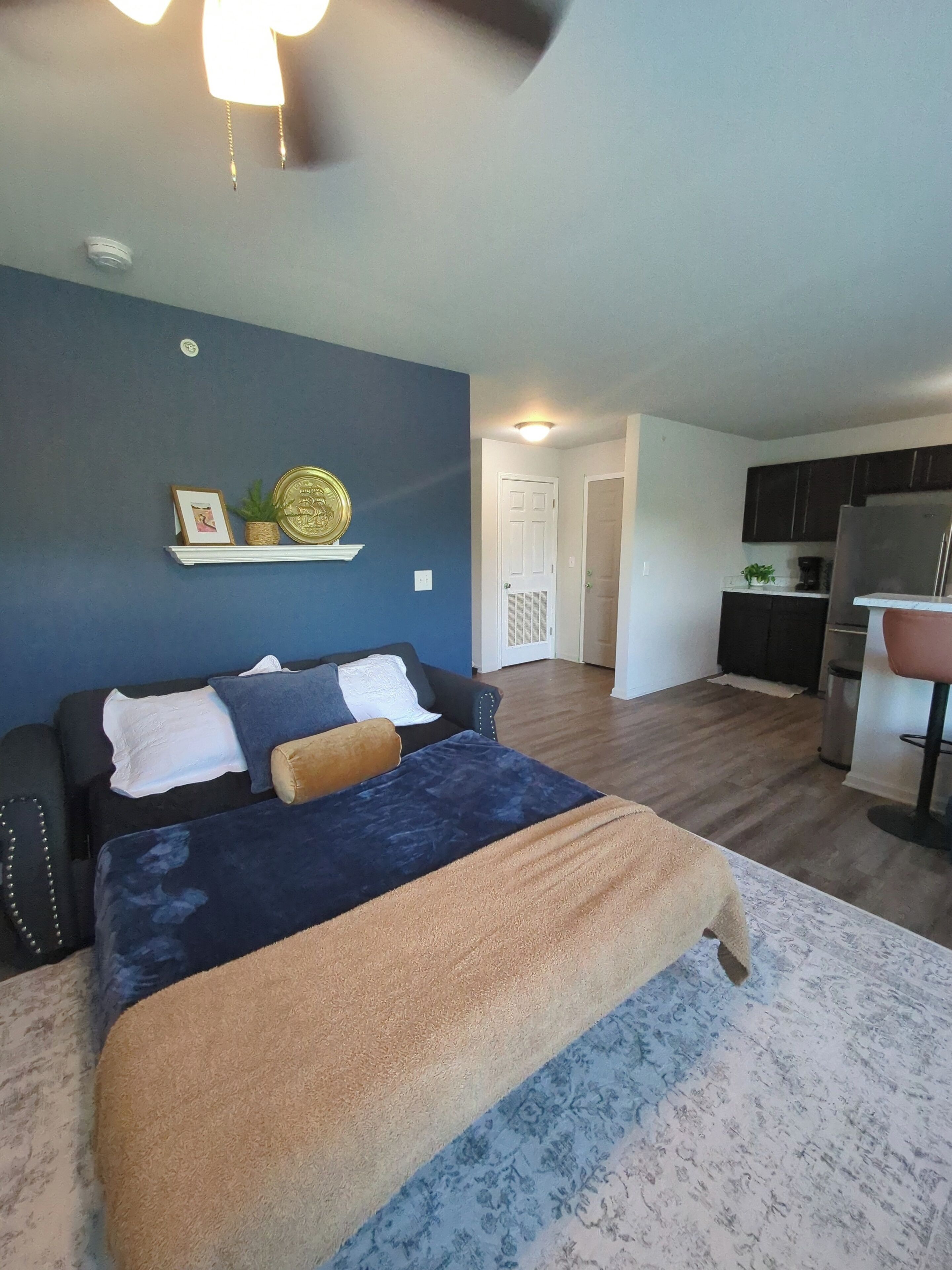 A bedroom with a bed, a nightstand, a wall-mounted shelf with decorative items, and a door leading to a hallway.
