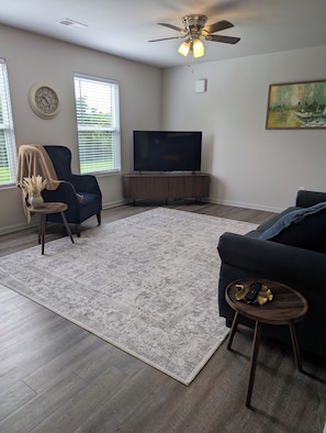 Una sala de estar con televisor, ventilador de techo, sofá, silla y alfombra.