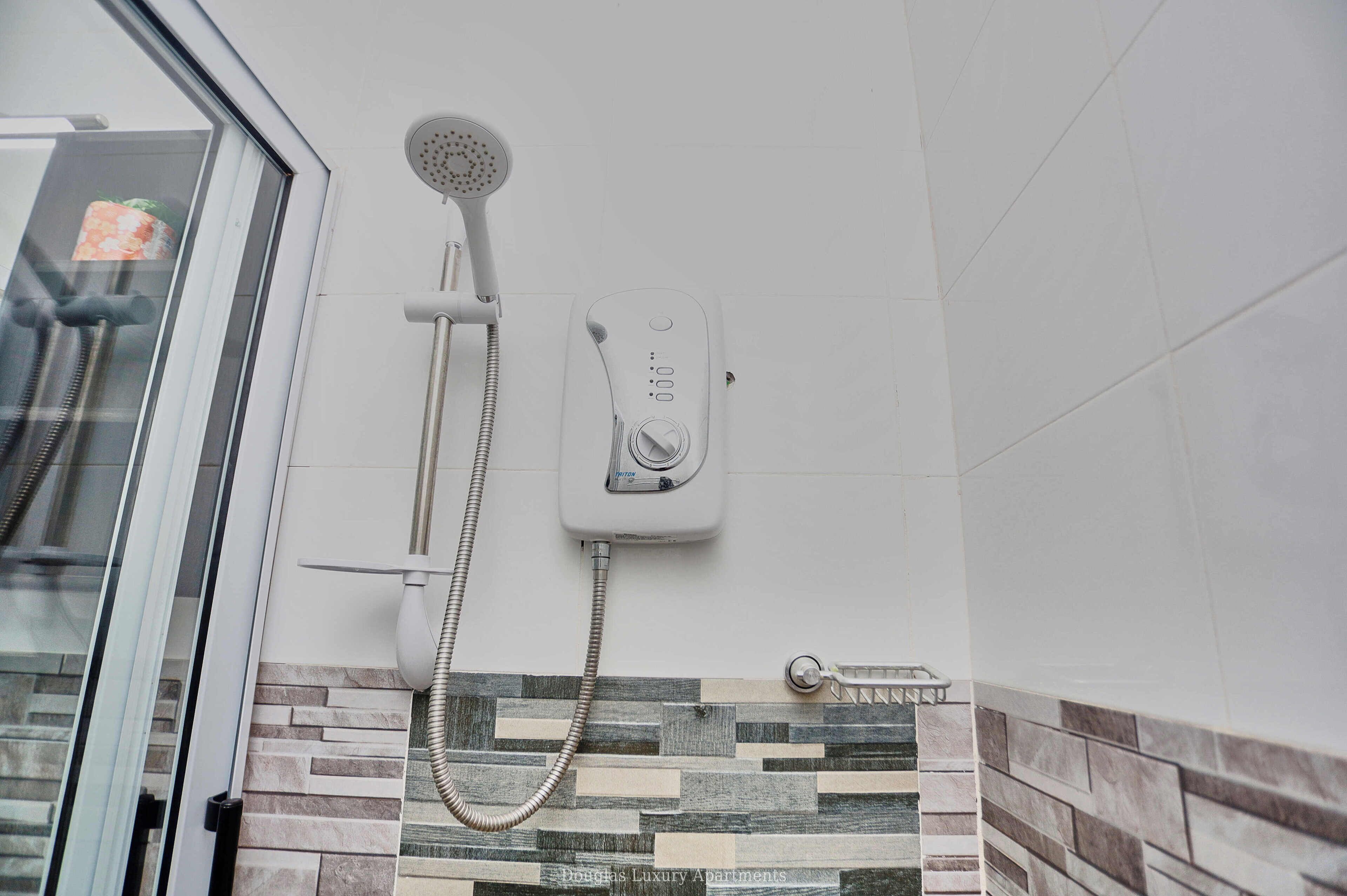 Een badkamer met een douche, een bedieningspaneel aan de muur en een betegelde spatwand.