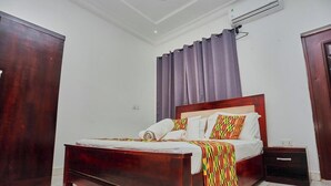Quarto com cama de madeira, mesa de cabeceira, guarda-roupa e janela com cortinas.