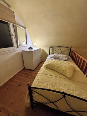 Ein Schlafzimmer mit Bett, Kommode, Spiegel und Fenster.