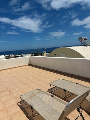 Eine Dachterrasse mit zwei Liegestühlen, einer Satellitenschüssel und Blick auf das Meer.