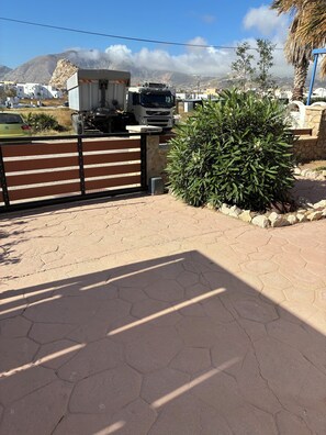 A paved area with a gated entrance, a parked truck, and a bush. - Family friendly house with sea view in Santorini (Σαντορίνη)