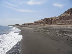 Ein Strand mit dunklem Sand, Wellen und felsigen Klippen.