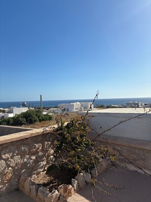 Eine Dachterrasse mit Blick auf das Meer, Steinmauern und moderne Gebäude im Hintergrund.