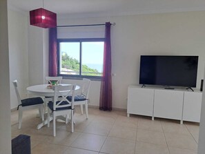 A dining area with a table and chairs, a television on a cabinet, and a window with curtains. - Apartment SEA & OLD TOWN VIEWS (Albufeira)