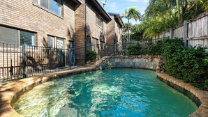 Ein Pool mit Steinrand, umgeben von einem Backsteinhaus mit Metallzaun.