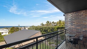 Ein Balkon mit Blick auf das Meer, eine Backsteinmauer und ein kleiner Tisch mit Stühlen.
