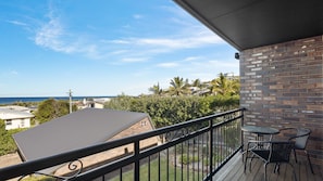 A balcony with a view of the ocean, a brick wall, and a small table with chairs.
