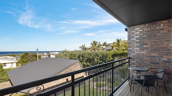Ein Balkon mit Blick auf das Meer, eine Backsteinmauer und ein kleiner Tisch mit Stühlen.