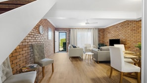 Ein modernes Wohnzimmer mit Backsteinwand, Deckenventilator und Fernseher.