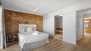 Ein modernes Hotelzimmer mit Ziegelwand, einem Bett mit weißer Bettwäsche, einem Deckenventilator und Blick ins Badezimmer.