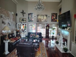 Uma sala de estar ampla com lareira, sofás de couro, um candelabro e diversas obras de arte.