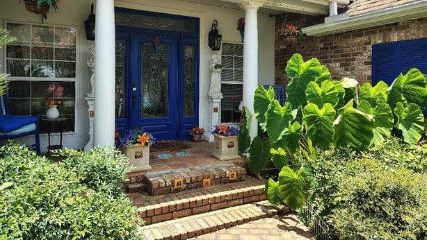 Una casa con puerta principal azul, columnas blancas y porche de ladrillo.