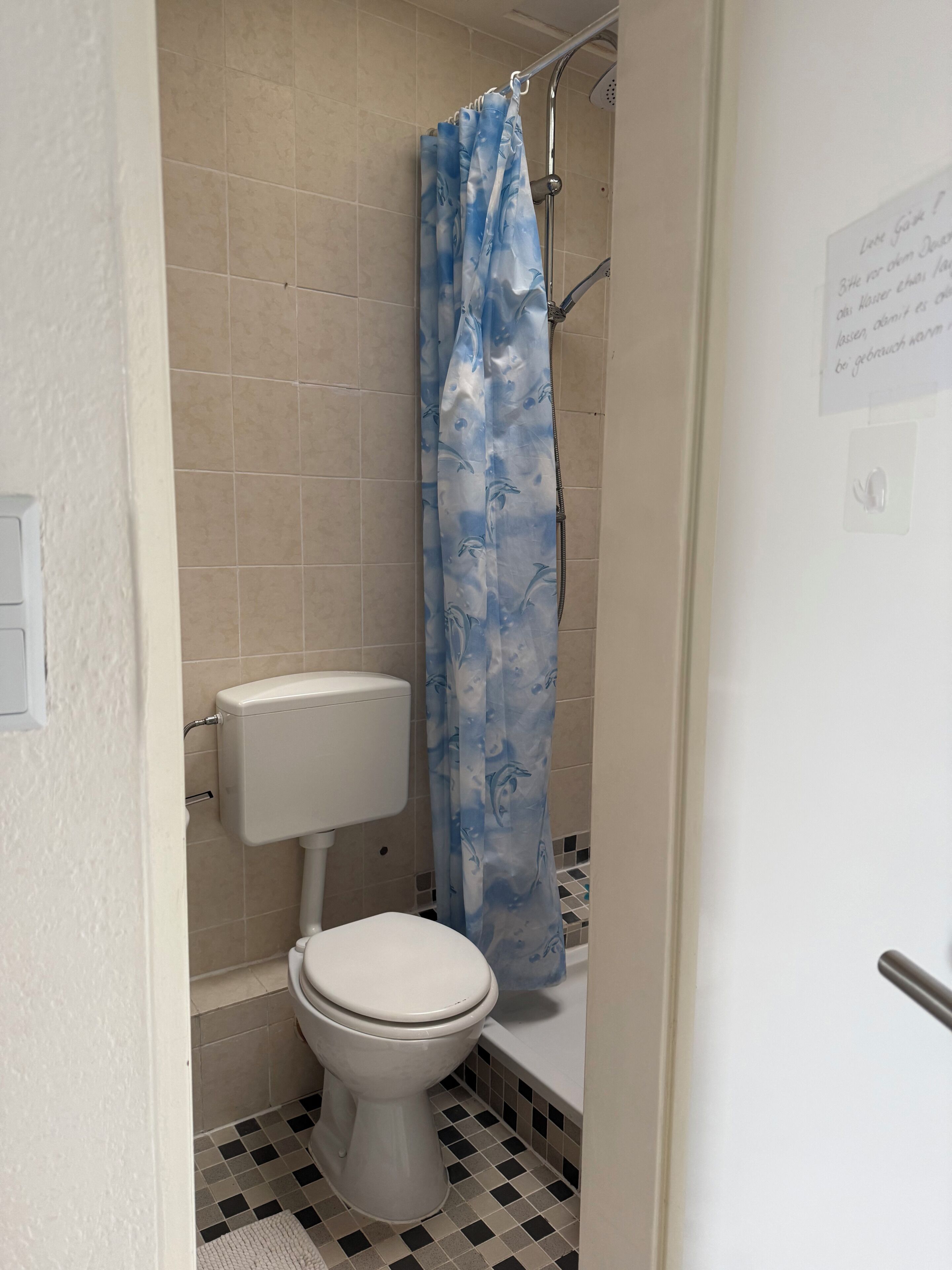 A bathroom with a toilet, shower curtain, and tiled floor.