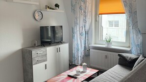 Ein modernes Wohnzimmer mit einer Couch, einem Couchtisch, einem Fernseher und einem Fenster mit Vorhängen.