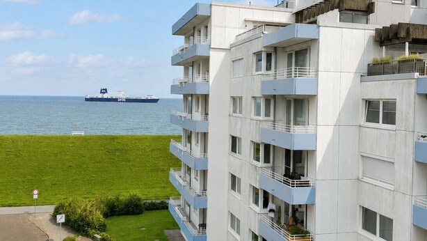 Ein mehrstöckiges Gebäude mit Balkonen, einer Rasenfläche und Blick auf das Meer.