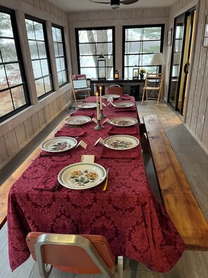 Ein Esszimmer mit einem langen Tisch, gedeckt für sechs Personen, großen Fenstern und Blick auf Bäume.