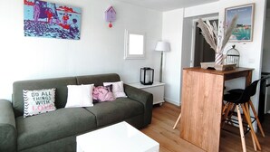 Un soggiorno con un divano verde, un tavolino da caffè bianco, un comodino in legno e una ventola a soffitto.