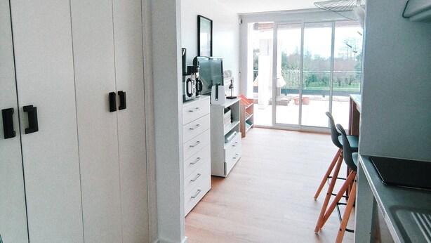 Una cucina moderna con mobili bianchi, un'area pranzo con tavolo e sedie, e un'ampia porta-finestra che dà su un balcone.