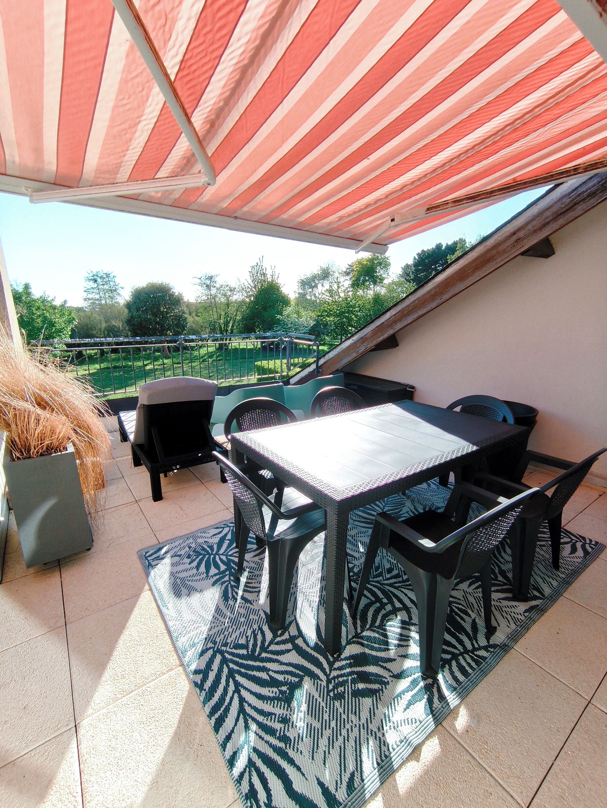 An outdoor patio with a table and chairs, a striped awning, and a view of a garden.