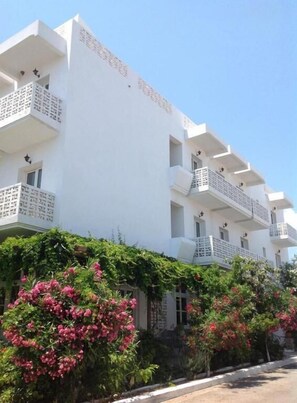 A multi-story building with balconies, surrounded by lush greenery and flowering plants. - ADAMANTIA HOTEL (Samos)