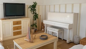 A living room with a television, piano, and a table with a plant and a rolled-up mat.