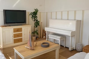Ett vardagsrum med en tv, ett piano och ett bord med en växt och en hoprullad matta.