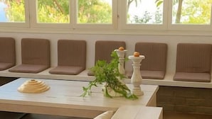 A room with a large window, a seating area with cushioned benches, a table with a plant, and a small table with a candle.