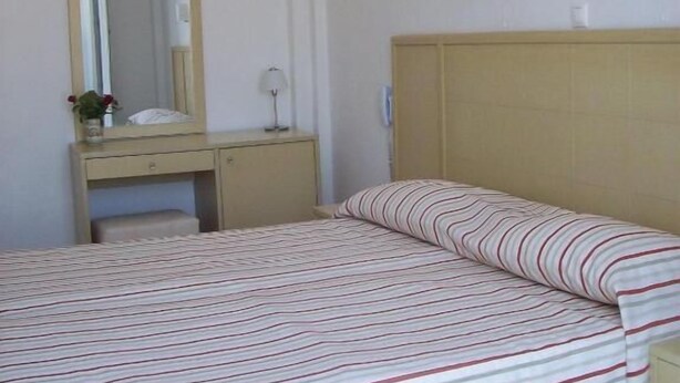 A bedroom with a bed, a bedside table, a mirror, and a wall-mounted light fixture.