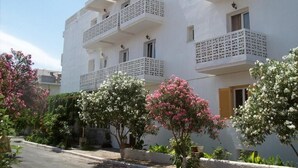 A multi-story building with balconies, a paved driveway, and flowering trees.