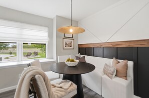 A modern living room with a round table, a sofa, a hanging light fixture, and a window with a view of the outdoors.
