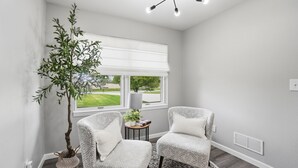 A room with two patterned chairs, a potted plant, a small table with a plant, and a large window with a view of the outdoors. - LUXURY COUNTRY RETREAT ~ HEATED POOL, PICKLEBALL COURT, FIRE PIT & COUNTRY VIEWS (Wauseon)