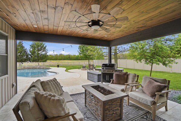 A covered patio with a pool, outdoor seating, and a grill area.