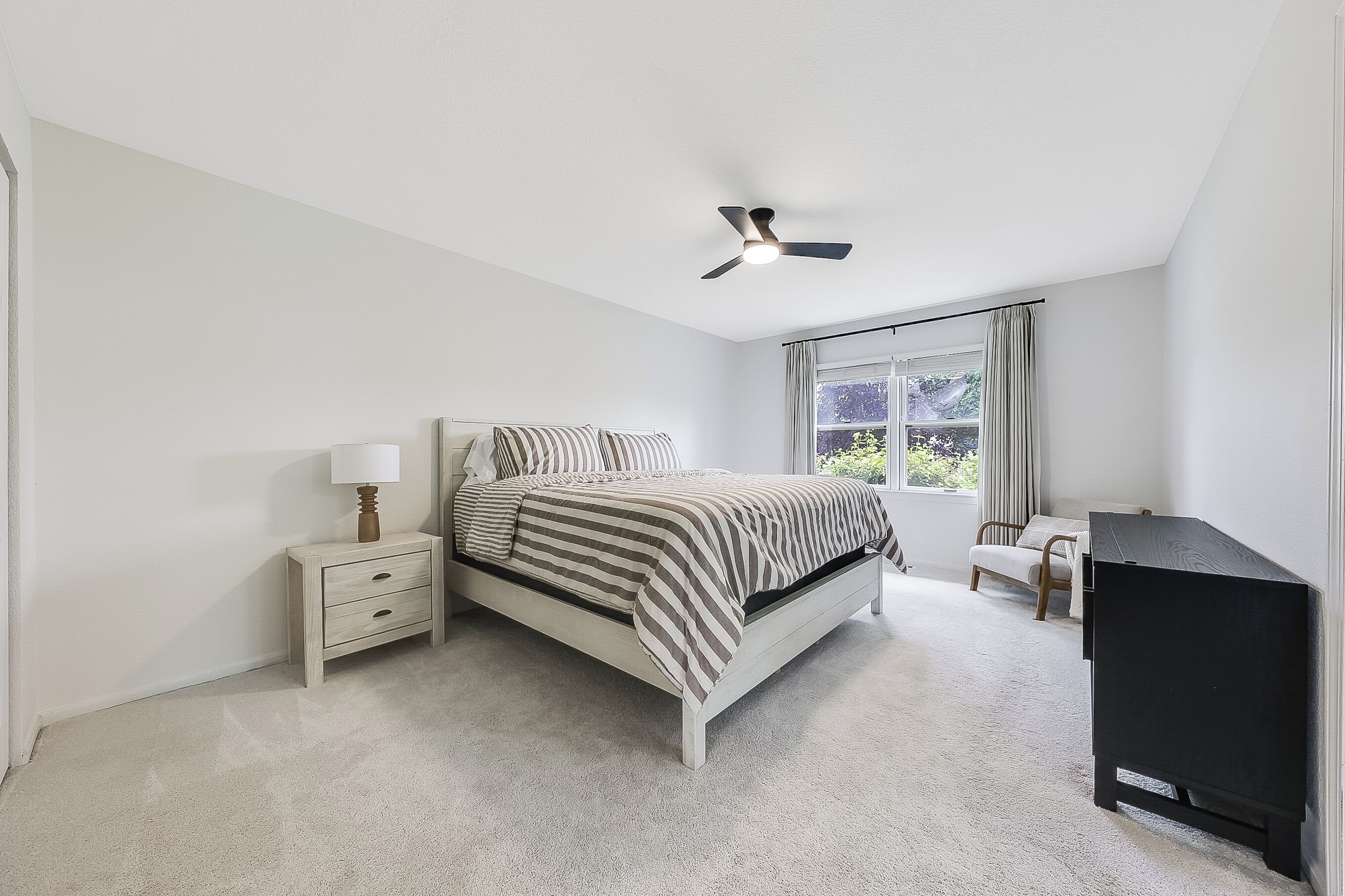 A bedroom with a bed, bedside tables, a ceiling fan, a window with curtains, and a television.