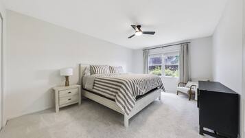 A bedroom with a bed, bedside tables, a ceiling fan, a window with curtains, and a television.