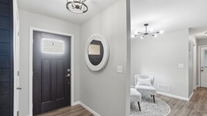 A hallway with a dark door, a round mirror, a ceiling fan, and a patterned rug. - LUXURY COUNTRY RETREAT ~ HEATED POOL, PICKLEBALL COURT, FIRE PIT & COUNTRY VIEWS (Wauseon)